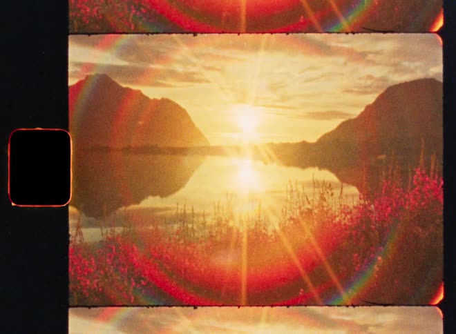 A vintage film strip captures a dramatic lens flare during a golden sunset over a calm mountain lake with wildflowers in the foreground