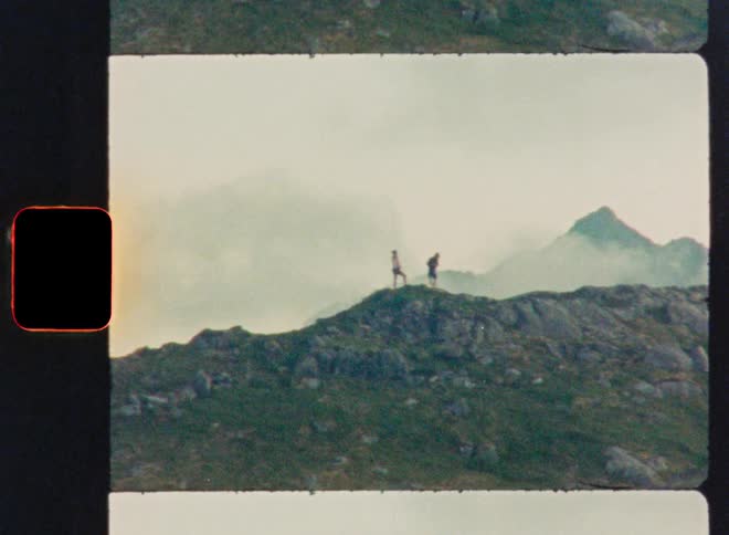 A Super 8mm film captures two hikers enjoying the vast, misty view from a mountain peak in the distance