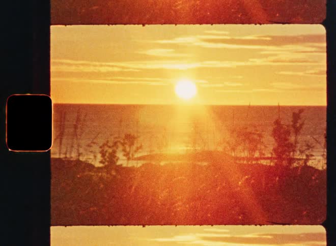 A nostalgic, grainy 8mm film captures the warm glow of the sun slowly setting over the ocean horizon