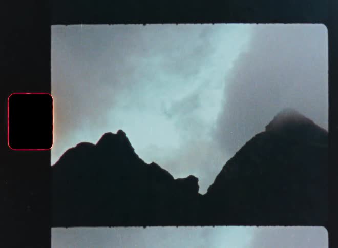A static shot on a vintage film strip reveals a moody mountain silhouette against a foggy sky