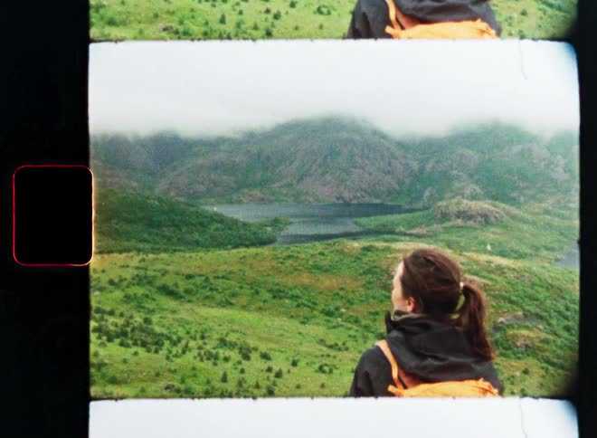 A female hiker with a backpack gazes at a misty mountain valley landscape in a vintage 8mm film style cinemagraph