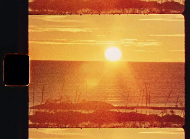 A vintage-style film shot captures a beautiful golden sunset over the ocean with silhouetted sand dunes in the foreground
