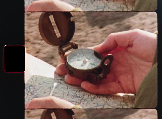 A vintage 8mm film style clip shows a close-up of a person holding a compass over a map
