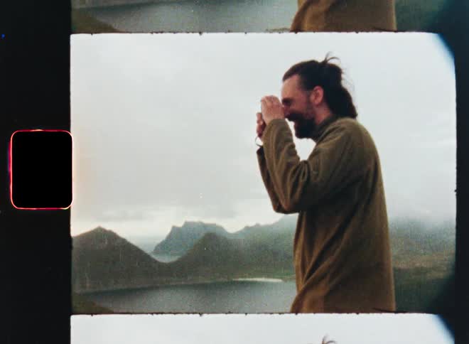 A smiling man with a beard photographs a stunning mountain and sea landscape in a vintage, film-style clip