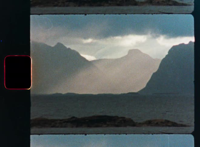 Vintage film captures a moody and atmospheric view of a misty mountain fjord with a small rocky island