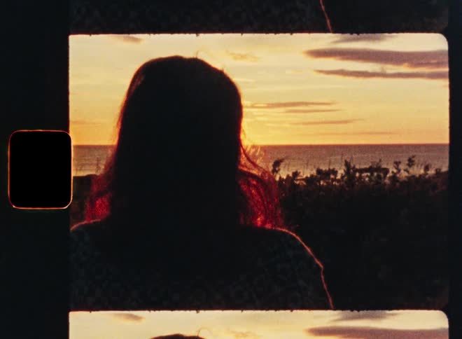 Vintage 8mm film captures the silhouette of a woman watching a golden sunset over the tranquil ocean