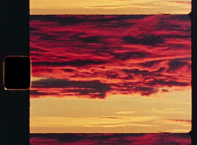 A vintage 8mm film scan of a dramatic red sunset with dark, textured clouds over a golden horizon
