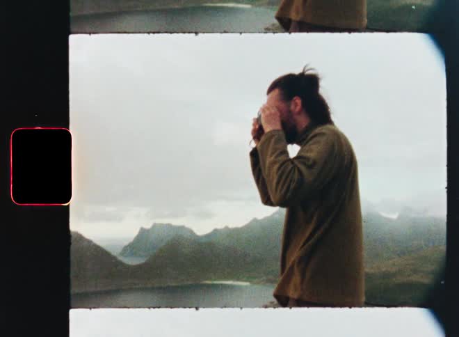 A nostalgic film strip aesthetic frames a photographer capturing the stunning mountain and fjord landscape on a cloudy day