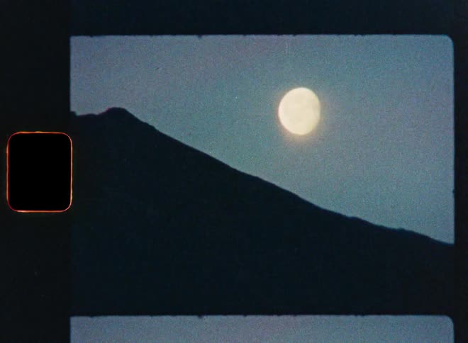 A grainy vintage film scan shows the full moon rising over a silhouetted mountain at night