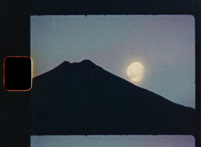 A vintage 16mm film scan captures the majestic silhouette of a mountain with a full moon in the background