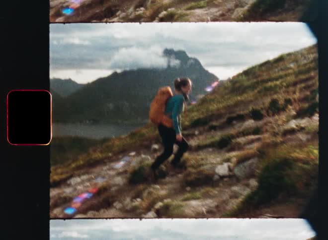 A female hiker with an orange backpack climbs a steep, rocky mountain trail with a beautiful fjord in the background, captured in a vintage film style