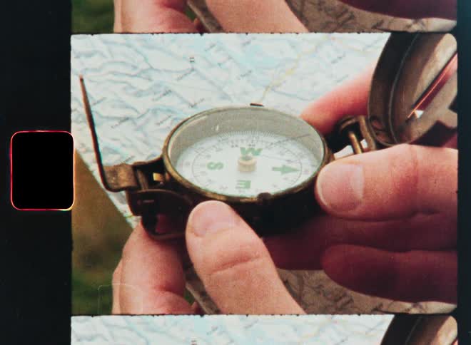A close-up shot of a person's hands holding a vintage-style brass compass over a paper map