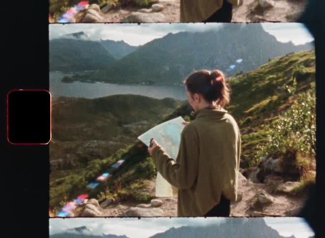 A vintage film shot of a young female hiker looking at a map while standing on a mountain overlooking a scenic valley