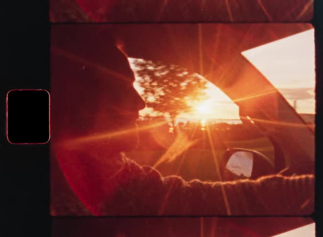 A man drives during a golden hour sunset, captured on vintage film with beautiful sun flares