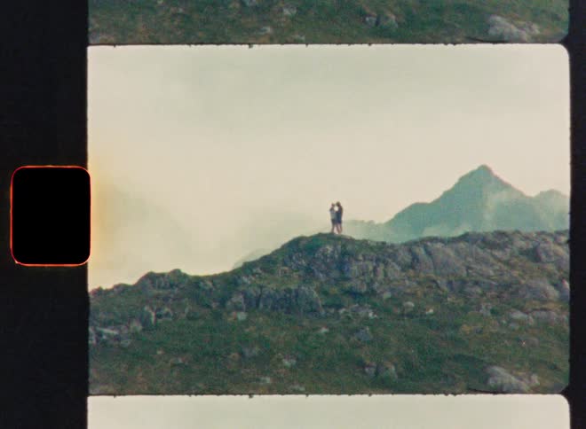 An archival film scan captures a couple standing together on a majestic, misty mountain top