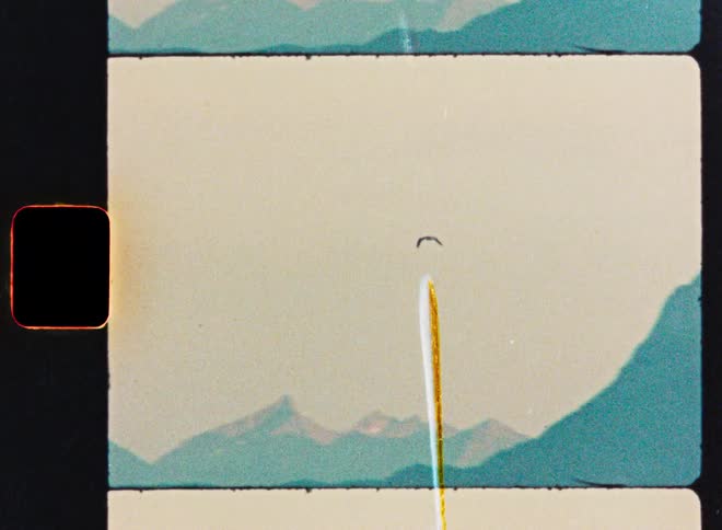 A vintage 8mm film scan shows a single bird soaring gracefully over a distant, hazy mountain range by the sea
