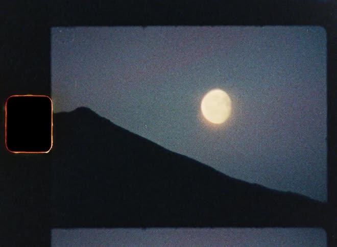 A vintage 8mm film captures the serene beauty of a full moon rising over a silhouetted mountain at twilight