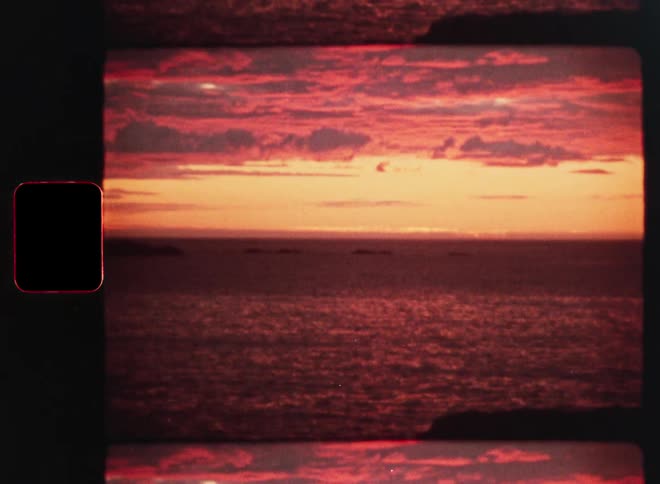A beautiful sunset with red clouds reflects on the ocean's surface in this vintage film clip