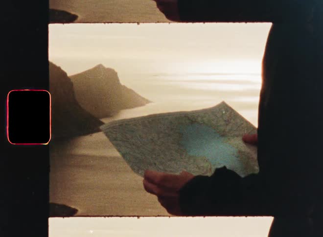 A person holds a map while overlooking a vast, mountainous coastal landscape in this vintage, film-strip style clip