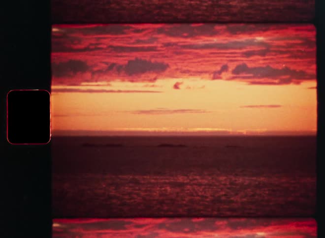 A dramatic fiery red sunset with glowing orange hues over the ocean, captured on vintage film