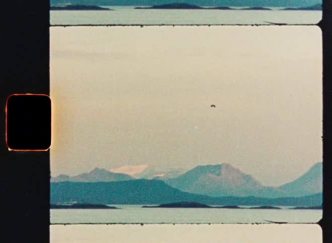 A vintage 8mm film strip shows a slow pan across a serene mountain range over a calm body of water