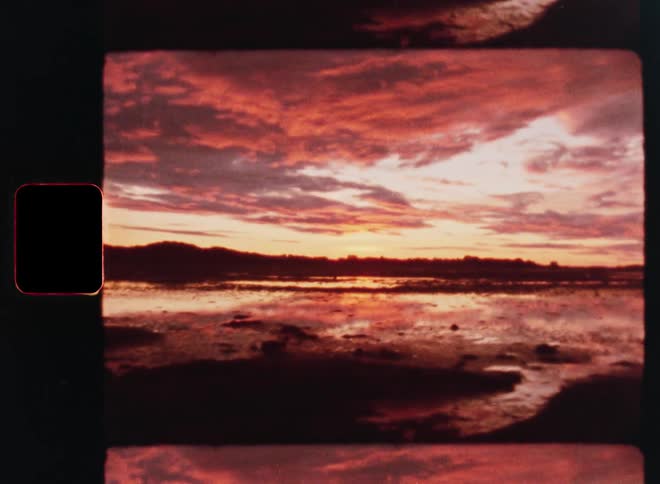 A beautiful, fiery red sunset reflects over a calm body of water, captured on nostalgic vintage film