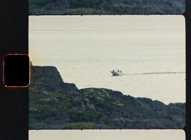 Vintage Super 8 footage shows a motorboat traveling across the water near a rocky coastline