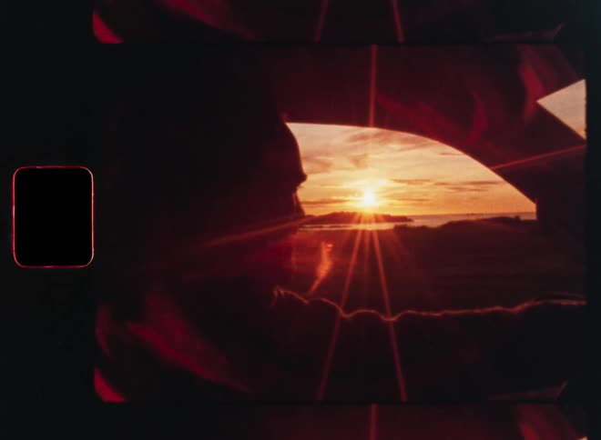 A person's silhouette is framed inside a car window while they watch a stunning sunset over the ocean, captured on dreamy vintage film