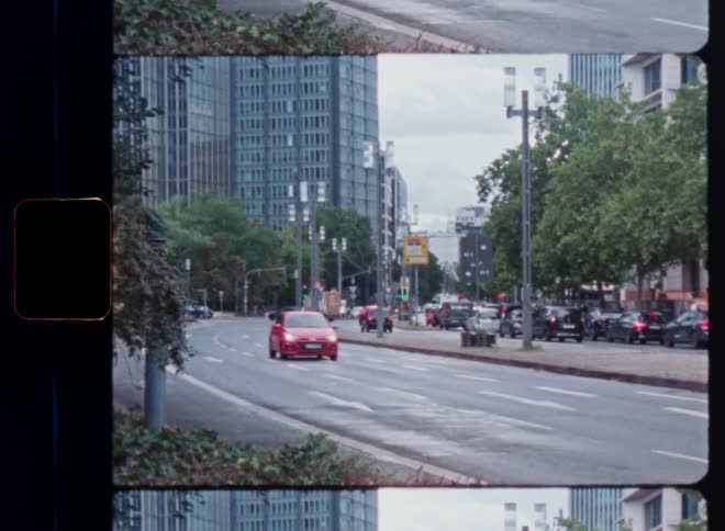 A vintage Super 8mm film scan effect reveals a red car driving down a busy city street