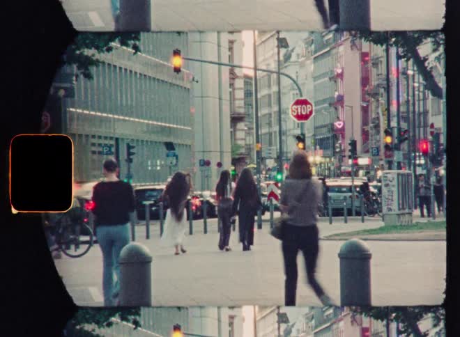 A grainy Super 8 film captures a bustling city street corner with pedestrians and changing traffic lights