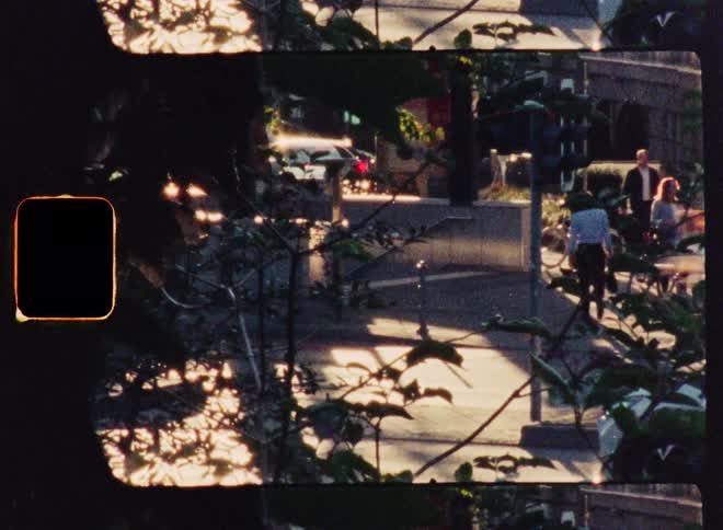 Vintage super 8 film captures a bustling city street corner with pedestrians and traffic during a sunny golden hour