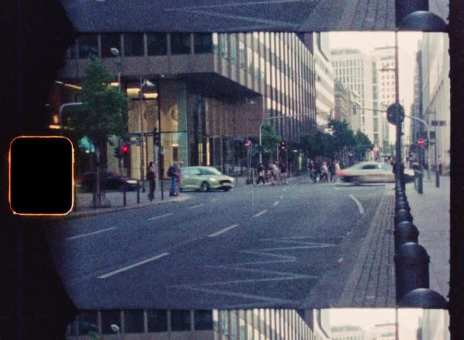 A vintage, grainy film-style timelapse captures the flow of traffic and pedestrians on a modern city street at dusk