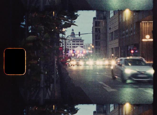 A grainy, vintage split-screen shot captures cars with bright headlights driving on a wet city street at night