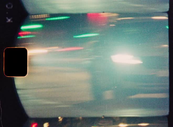 Dreamy vintage film footage captures abstract, blurred streaks of colorful city traffic lights at night