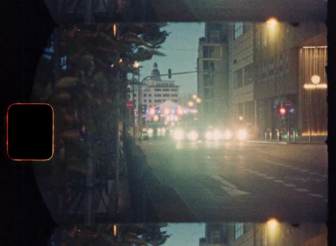 Grainy vintage film captures a dreamy, hazy view of city street traffic at dusk
