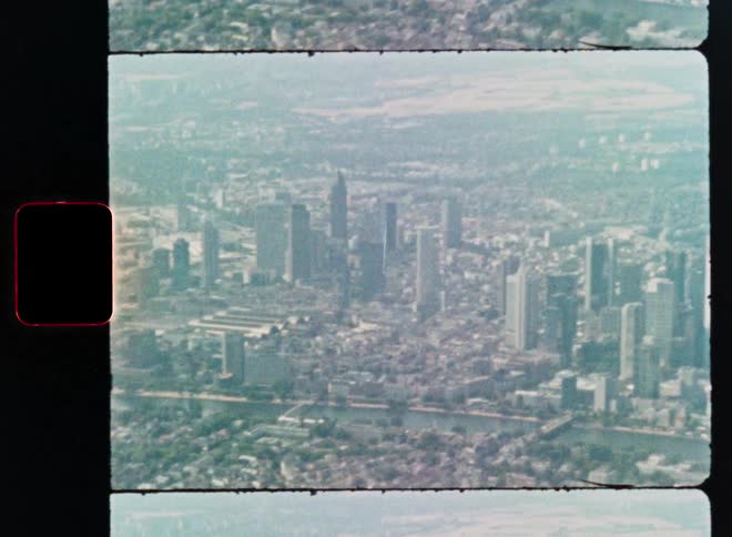 A vintage scanned Super 8 film captures a hazy aerial view of the Frankfurt, Germany city skyline and the Main river