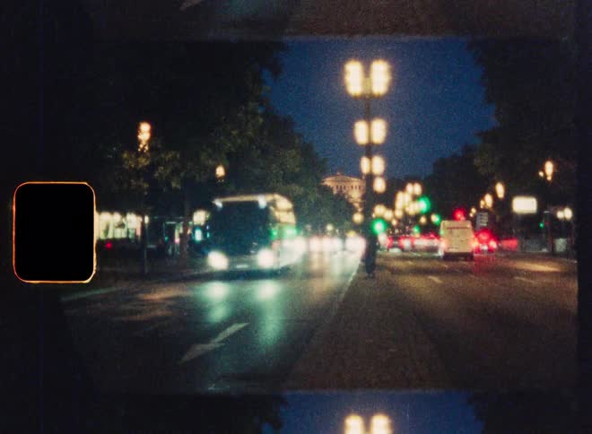 A vintage, blurry 8mm film shot of a man in a suit walking along a busy city street at night as traffic passes by
