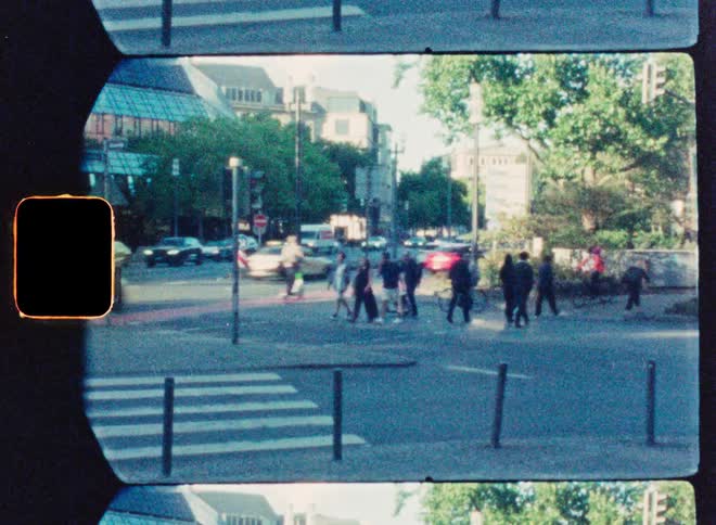 A retro, film-strip-style video shows pedestrians crossing a busy city intersection as traffic passes by