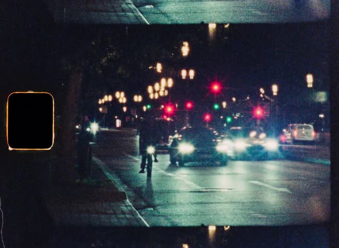 Dreamy, vintage film captures cars and a cyclist on a busy city street at night