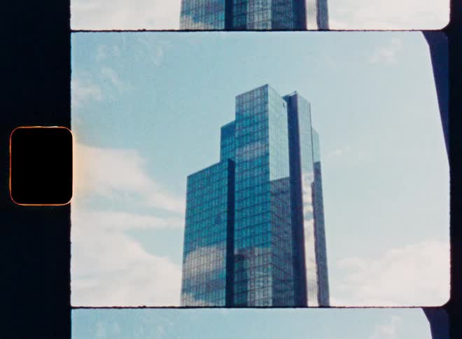 A modern glass skyscraper seen through a vintage 8mm film scan effect with light leaks and passing clouds