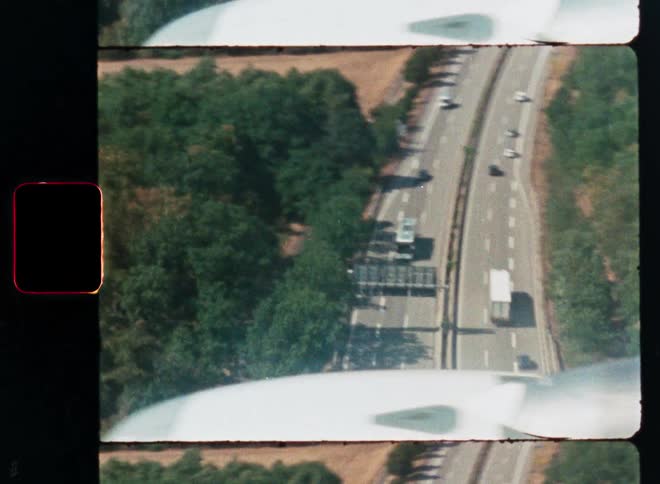 A vintage 8mm film captures an aerial view of traffic on a highway from an airplane window