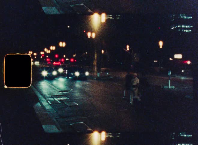 Vintage 8mm film captures the bustling city nightlife with blurry, streaking car lights on a busy street