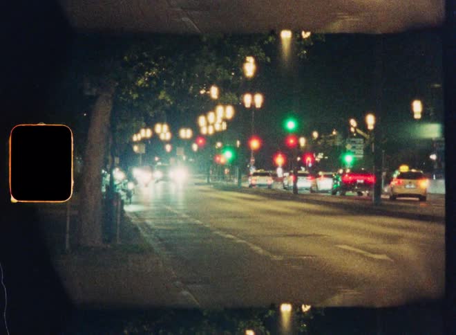 Vintage film captures a dreamy, out-of-focus city street with traffic moving under streetlights and traffic signals at night