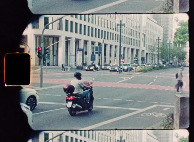 A vintage film time-lapse captures the motion of cars, cyclists, and pedestrians at a busy city street intersection