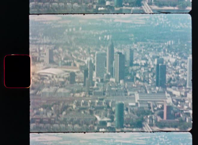 An archival 8mm film scan captures a hazy, aerial perspective of the Frankfurt, Germany cityscape and river