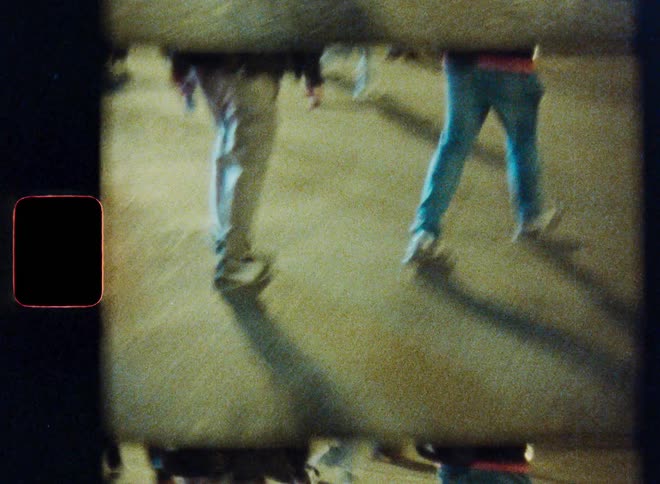 Abstract Super 8 footage shows distorted images of pedestrians and a cyclist on a sidewalk at night