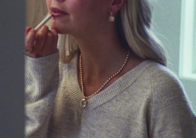 A close-up shot of a blonde woman wearing a cozy sweater applying lip liner to her lips