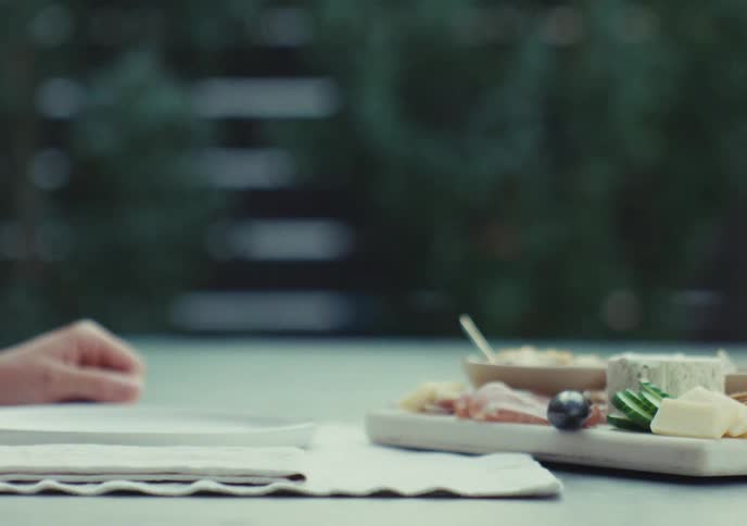 A woman's hand swirls and lifts a glass of red wine while sitting at an outdoor table with a charcuterie board