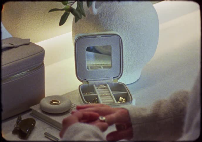Vintage-style footage of a woman's hands selecting a ring from a travel jewelry box on her vanity