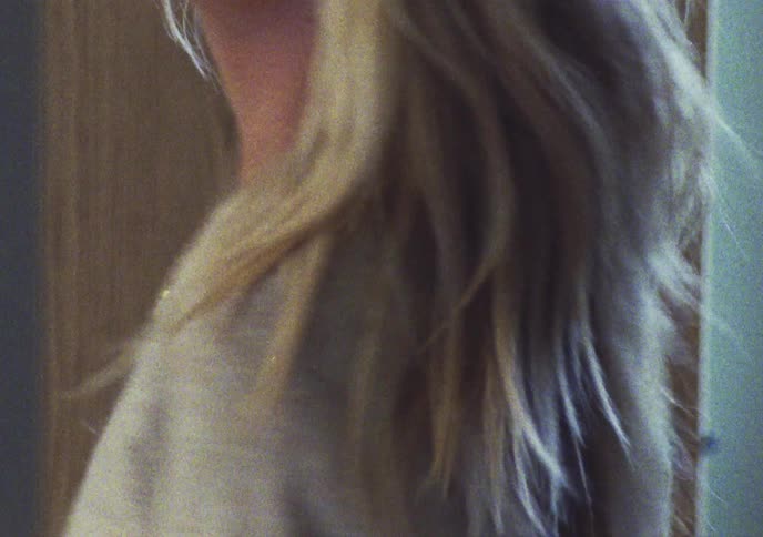 Dreamy film shot of a blonde woman running her hand through her hair before walking away